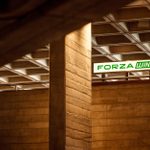A brightly lit sign for Forza Wine sits overlooking a balcony within the concrete architecture of the National Theatre