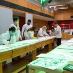A group of people in white hazmat suits drawing on big sheets of white paper.