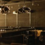 LASDUN Restaurant - a dark interior with table settings, large wall and pendant lights.
