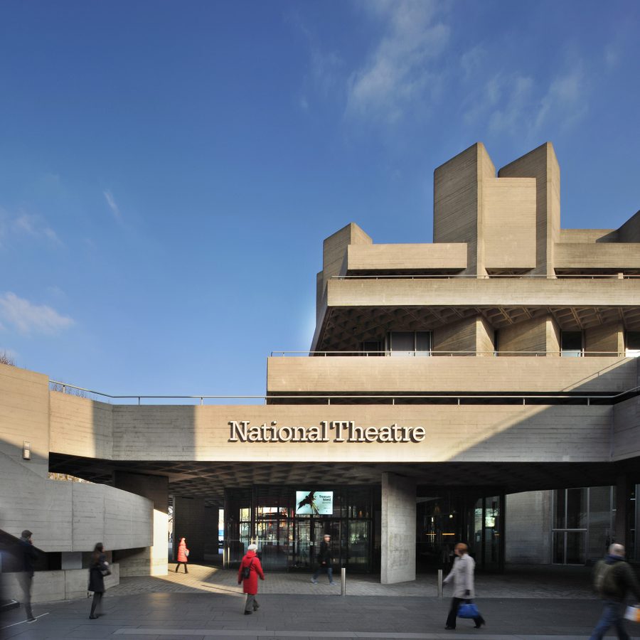National Theatre building, main entrance exterior with name in raised lettering on the lower terrace balcony and people walking in the square in front.