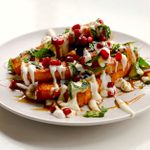 Halloumi fries with dressing, pomegranate pieces and herb leaves.